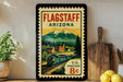A vintage-style postage stamp from Flagstaff, Arizona, featuring a train and mountains, is displayed on a shelf next to a wooden cutting board and some lemons.