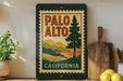 A framed vintage-style poster of the state of California, featuring a scenic landscape with mountains and a pine tree, is displayed on a shelf next to a wooden cutting board and some kitchen utensils.
