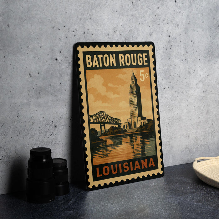 A vintage-style metal stamp depicting the city of Baton Rouge, Louisiana, with a bridge and a clock tower in the background.