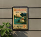 A vintage postage stamp for New Rochelle, New York, featuring a house, trees, and a body of water, mounted on a wall.