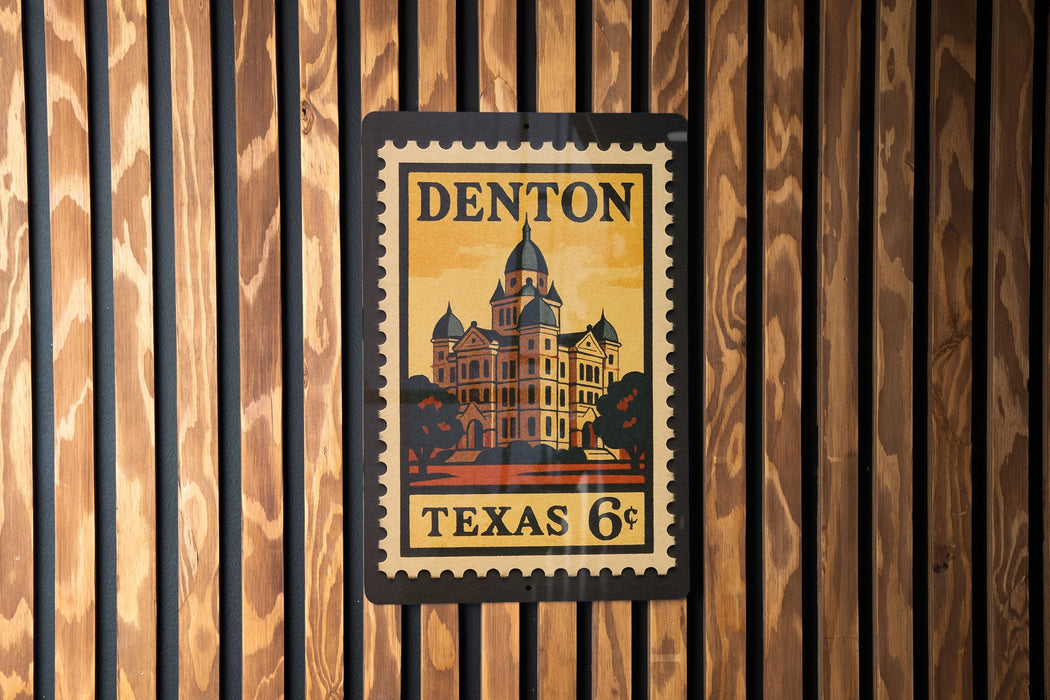 A vintage-style postage stamp from Texas, featuring a building with a dome, mounted on a wooden wall.