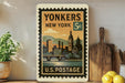 A vintage postage stamp from the United States, featuring an illustration of a cityscape with a clock tower, displayed on a shelf next to a wooden cutting board and some potted plants.