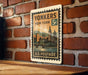 A vintage postage stamp from the United States, featuring a cityscape and a clock tower, is displayed on a brick wall.