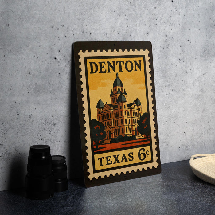 A metal sign with a vintage-style illustration of a building, placed on a table next to some black camera lenses.