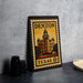 A metal sign with a vintage-style illustration of a building, placed on a table next to some black camera lenses.