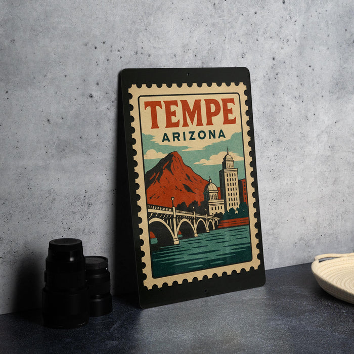 A framed poster of Tempe, Arizona, featuring a mountain and a bridge, is displayed on a countertop next to some black camera lenses.