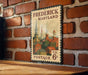 A vintage-style postage stamp from the United States of America, featuring a cityscape with buildings and spires, mounted on a brick wall.