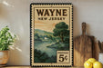 A vintage-style postage stamp from Wayne, New Jersey, featuring a scenic landscape with a river and trees, displayed on a shelf next to a wooden cutting board and some lemons.
