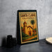 A framed poster of Santa Clara, California, featuring a church and palm trees, is displayed on a countertop.