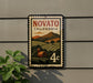 a vintage-style postage stamp with a landscape scene and a red barn, mounted on a wall.