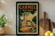 A vintage-style stamp depicting a town scene with a clock tower, surrounded by buildings and trees, with the text "CARMEL INDIANA" prominently displayed.