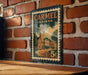 A vintage-style postage stamp from Carmel, Indiana, featuring a brick building and a clock tower, is displayed on a brick wall.