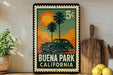 A vintage-style metal sign with a car illustration and the text "BUENA PARK CALIFORNIA" is displayed on a shelf, accompanied by a potted plant and a wooden cutting board.