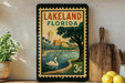 A framed vintage-style poster of Lakeland, Florida, featuring a swan in a pond and palm trees, is displayed on a shelf next to a wooden cutting board and a potted plant.