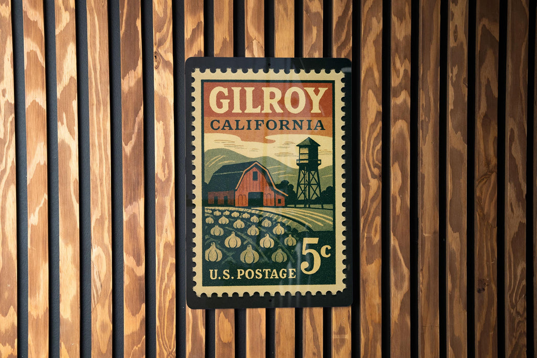A postage stamp from Gilroy, California, featuring a barn and a field with pumpkins, mounted on a wooden wall.
