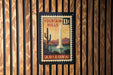A vintage postage stamp from Arizona featuring a fountain in the background, mounted on a wooden wall.