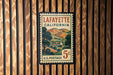A vintage postage stamp from Louisiana, California, featuring a landscape with hills and a church, mounted on a wooden wall.