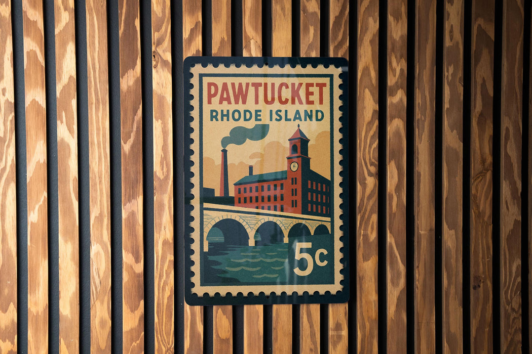 A vintage-style postage stamp from Pawtucket, Rhode Island, featuring a building and a bridge, mounted on a wooden wall.