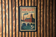 A vintage-style postage stamp from Pawtucket, Rhode Island, featuring a building and a bridge, mounted on a wooden wall.