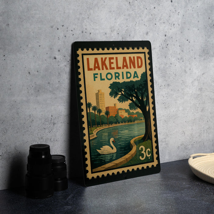 A vintage-style metal sign with the text "LAKELAND FLORIDA" and an illustration of a lake, palm trees, and a swan.