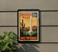 A framed poster of the Fountain Hills in Arizona, featuring a desert landscape with a tall spire and cacti, is displayed on a wall.