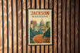 A vintage-style postage stamp from Jackson, Mississippi, featuring a cityscape and the text "FREVER USA" on a wooden background.