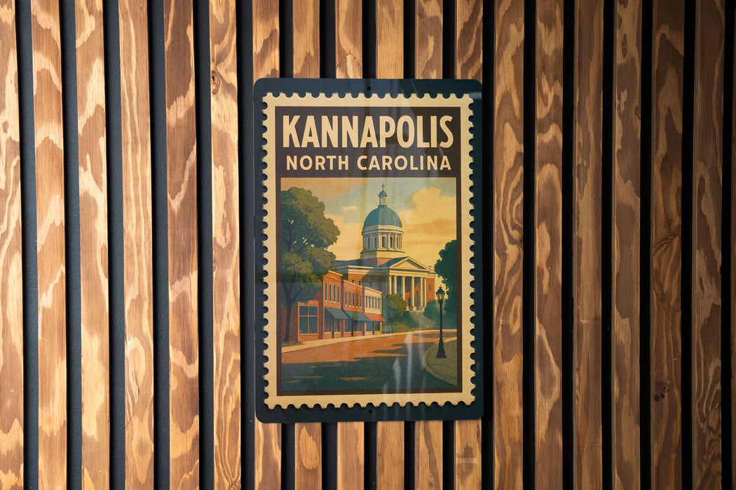 A vintage-style poster of the Kannapolis North Carolina landmark, featuring a building with a dome and a street scene, is displayed on a wooden wall.