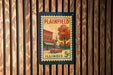 A vintage postage stamp from Illinois, featuring a building and a tree, is displayed on a wooden wall.