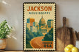 A framed vintage-style poster of Jackson, Mississippi, with a cityscape and a road, is displayed on a shelf next to a wooden cutting board and some lemons.