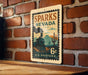 A vintage-style postage stamp from Sparks, Nevada, featuring a train and desert landscape, is displayed on a brick wall.