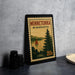A framed poster of Minnetonka, Minnesota, featuring a sailboat on a lake, is displayed on a countertop next to some black camera lenses.