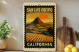 A framed vintage-style poster of San Luis Obispo, California, featuring a mountain landscape with a sunset in the background.