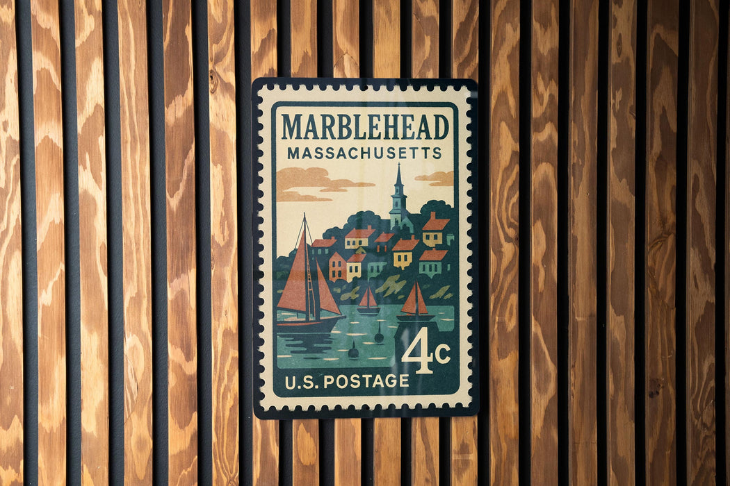 A vintage postage stamp from Massachusetts, featuring a town scene with sailboats and buildings, mounted on a wooden wall.