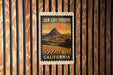 A framed poster of a mountain landscape with a sunset in the background, mounted on a wooden wall.