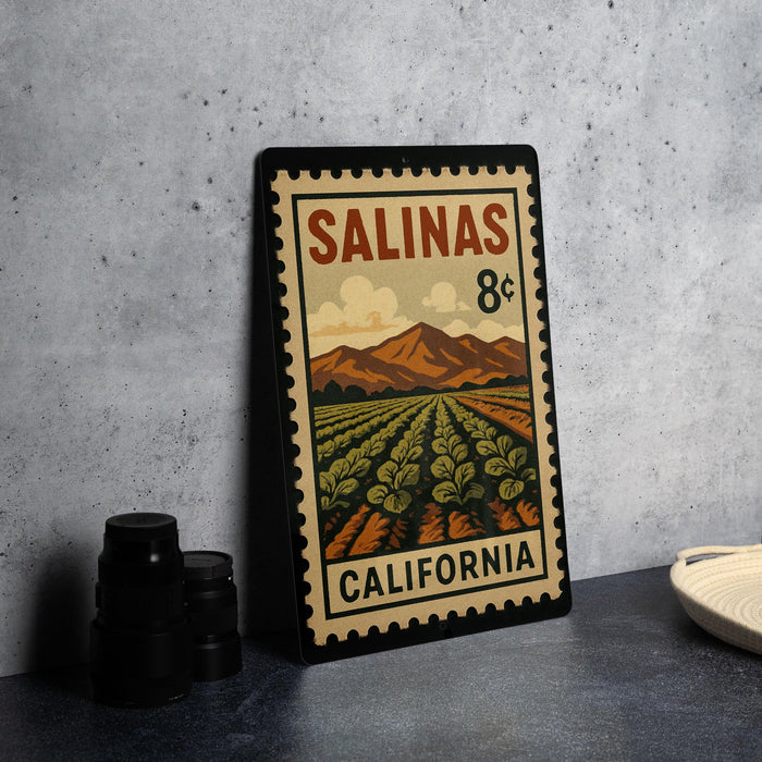 A metal stamp with a vintage-style illustration of a farm landscape and mountains, depicting the state of California.