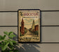 A vintage postage stamp from Massachusetts, featuring a cityscape with a church and buildings, mounted on a wall.