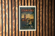 A vintage postage stamp from the United States of America, featuring a cityscape and a sailboat, is displayed on a wooden wall.