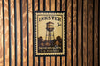 A vintage-style postage stamp featuring a water tower, mounted on a wooden wall.