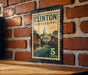 A metal sign with a vintage-style illustration of a town and a building, mounted on a brick wall.
