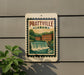 A sign for Prattville, Alabama, featuring a waterfall and buildings, mounted on a wall.