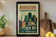 A vintage postage stamp from Boston, Massachusetts, featuring a cityscape and a church, is displayed on a shelf next to a wooden cutting board and some lemons.