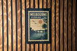A vintage postage stamp from Melbourne, Florida, featuring a sunset and palm trees, is displayed on a wooden wall.