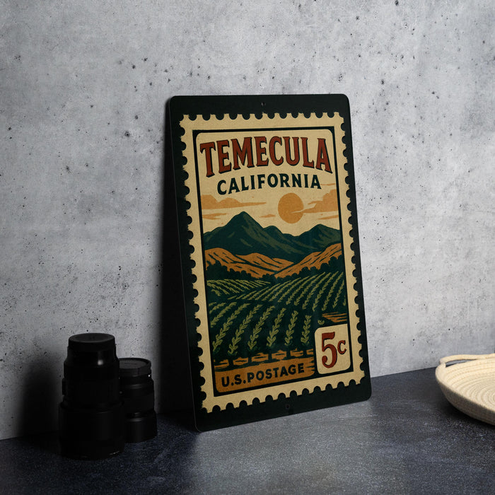 A framed vintage postage stamp from California, featuring a landscape with mountains and vineyards, is displayed on a table.