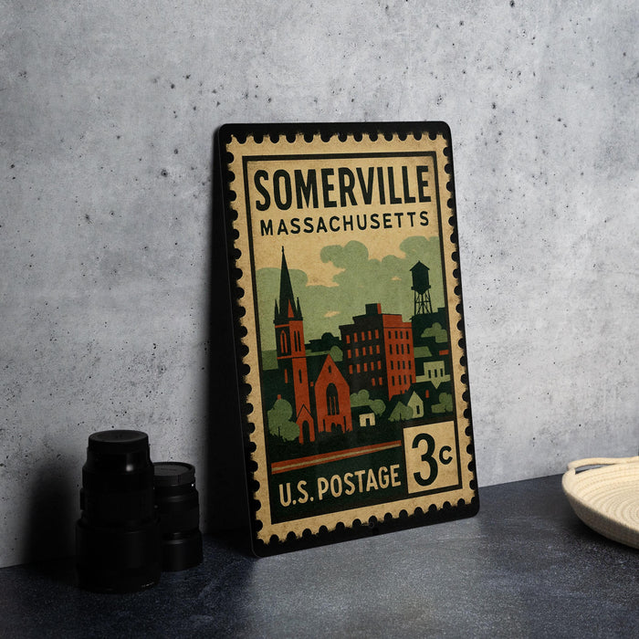 A vintage-style postage stamp from the United States, featuring an illustration of a town or city, placed on a countertop next to some camera equipment.