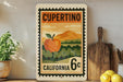 a vintage-style stamp or sign with an illustration of an apple and a landscape, placed on a shelf next to a wooden cutting board and some potted plants.
