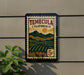 A vintage postage stamp from California, featuring a scenic landscape with mountains and vineyards, mounted on a wall.
