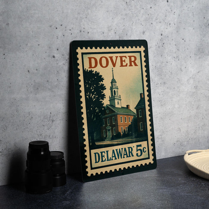 A vintage-style metal stamp depicting a building with a clock tower, placed on a countertop next to some black camera lenses.