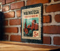A metal sign with a vintage-style illustration of a cityscape and a church, mounted on a brick wall.