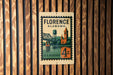 A vintage postage stamp from Florence, Alabama, featuring a bridge and a church, mounted on a wooden wall.