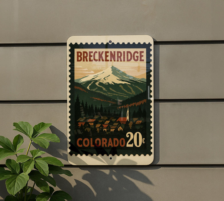 A vintage-style postage stamp depicting a mountain landscape with a small town in the foreground, mounted on a wall.